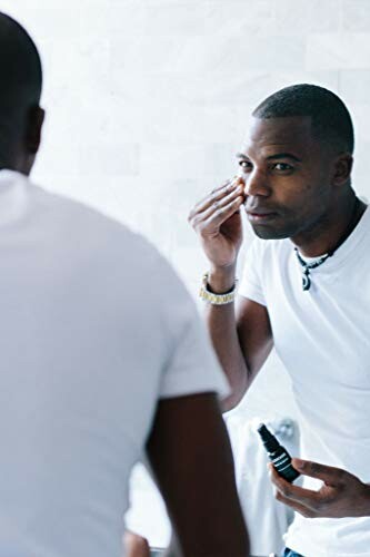 Man applying skincare product in front of mirror, highlighting the ease of use and application of Brickell's Restoring Eye Routine.